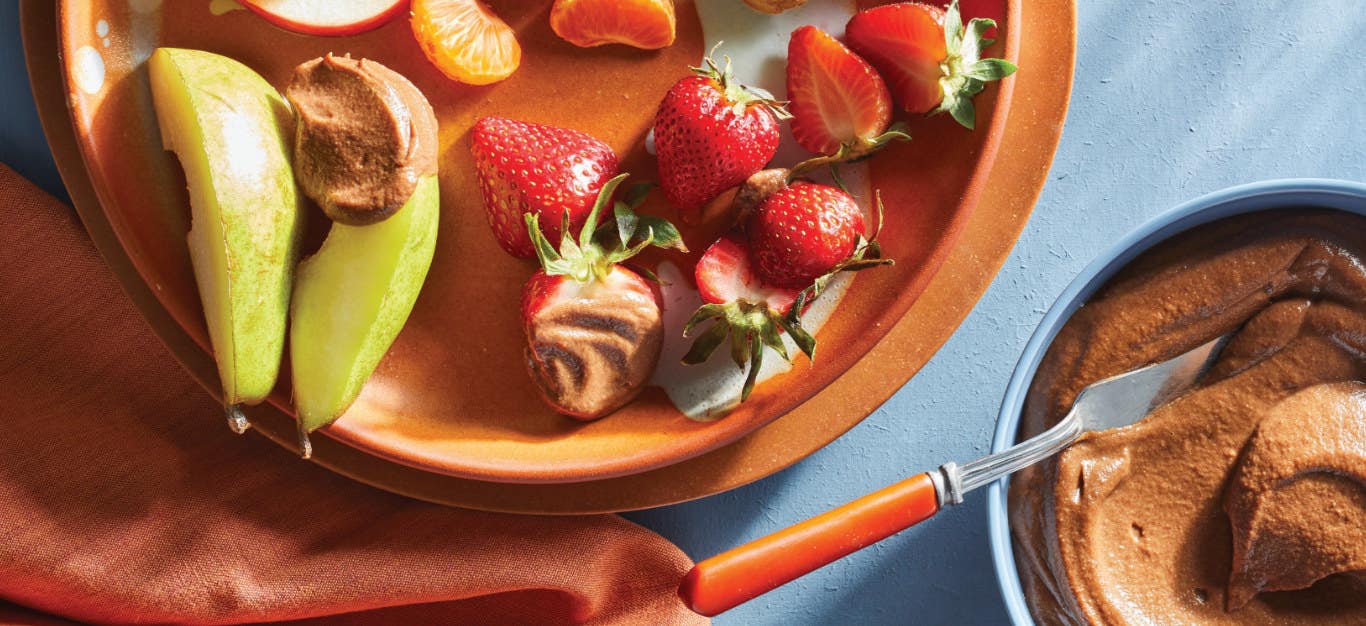 Raw Chocolate Caramel Dip in a small bowl next to a plate of bite-sized fruits