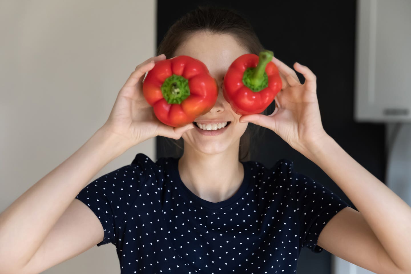 A young woman holds up two bell peppers to her eyes and smiles