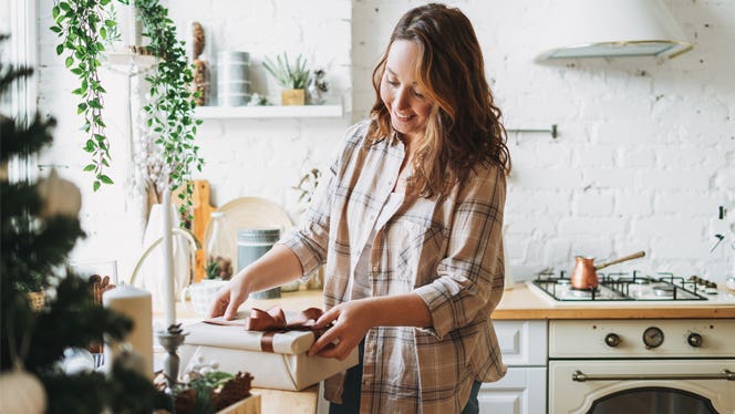 A woman stands in a brightly naturally lit kitchen wrapping presents