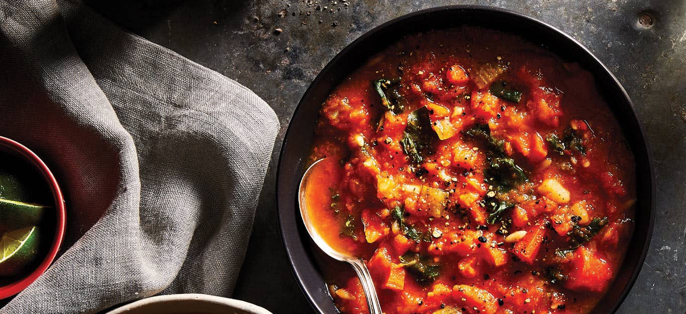 Carrot Ginger Soup with Orzo and Kale in a black bowl with a metal spoon against a gray countertop