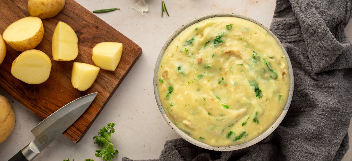 Good Garlicky Mashed Potatoes in a bowl next to a cutting board with potato wedges