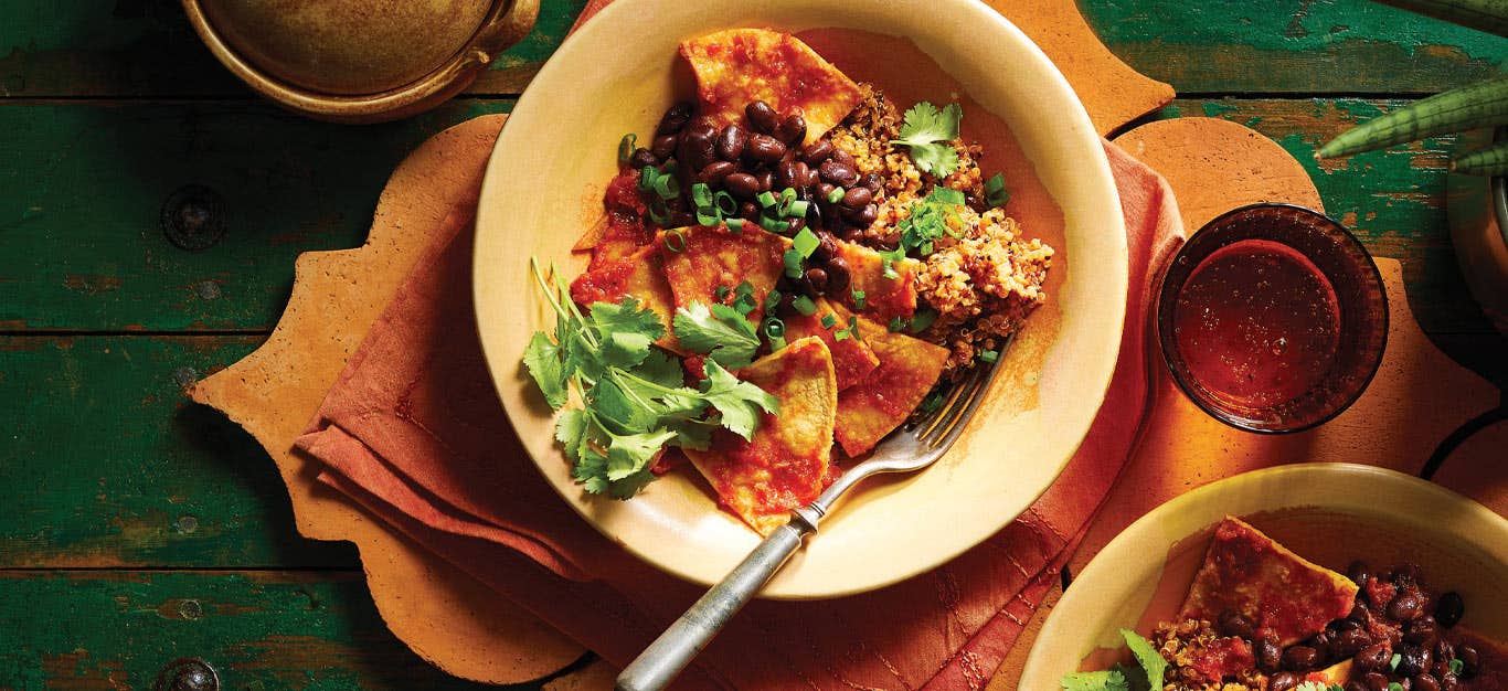 Vegan Chilaquiles in a cream colored bowl with a form set on an orange napkin against a green table