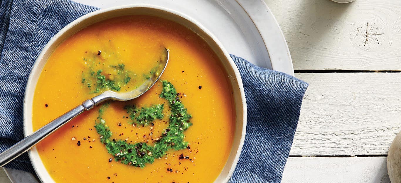 Butternut Bisque with Parsley Pistou in a white ceramic bowl resting on a blue cloth napkin