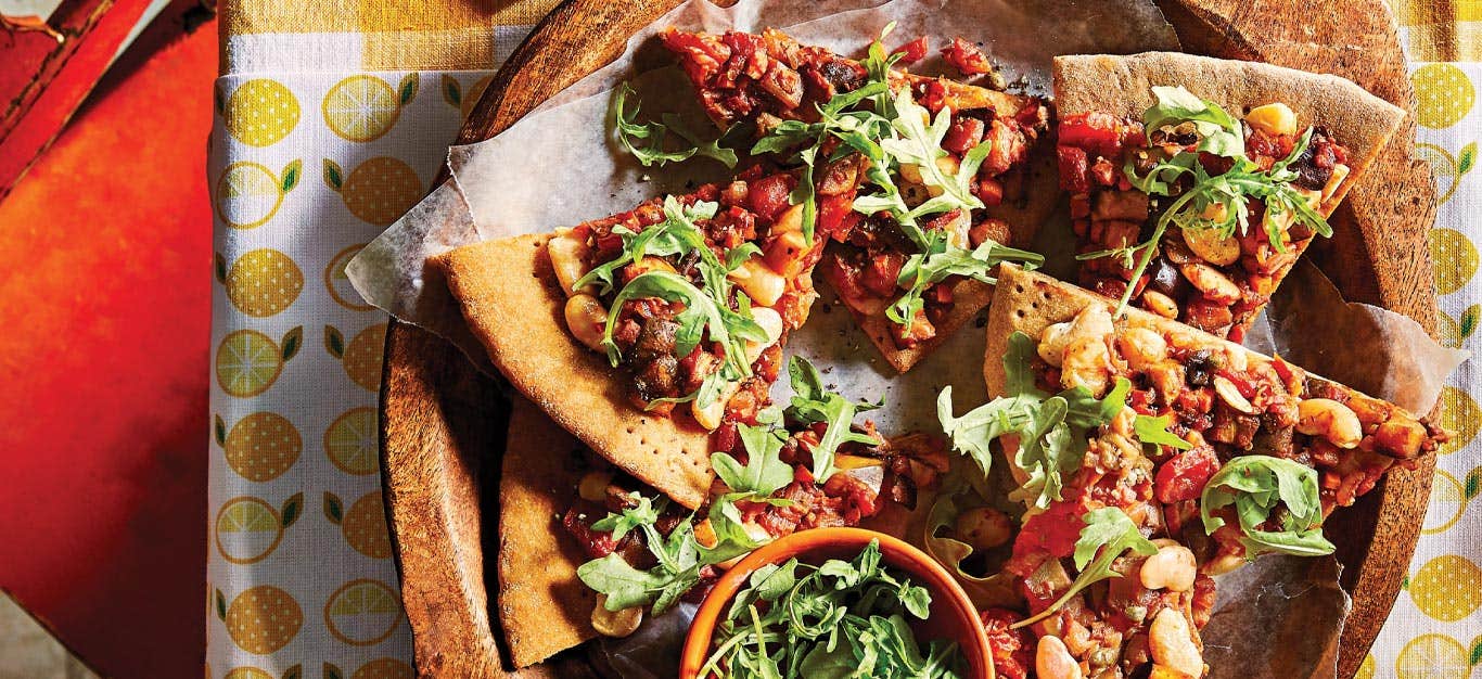 Caponata pizza on a wooden plate on top of a lemon-patterned tea towel