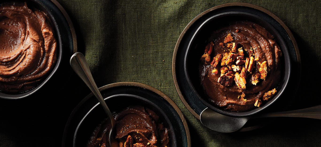 Creamy Sweet Potato Pudding topped with pecans in dark gray ceramic bowls against a green linen tablecloth