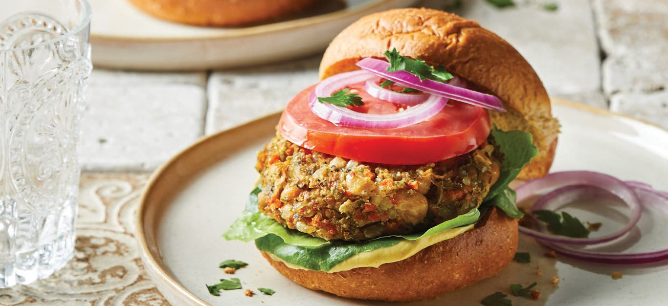 Tuscan White Bean Burgers topped with onion and tomato and on white ceramic plate