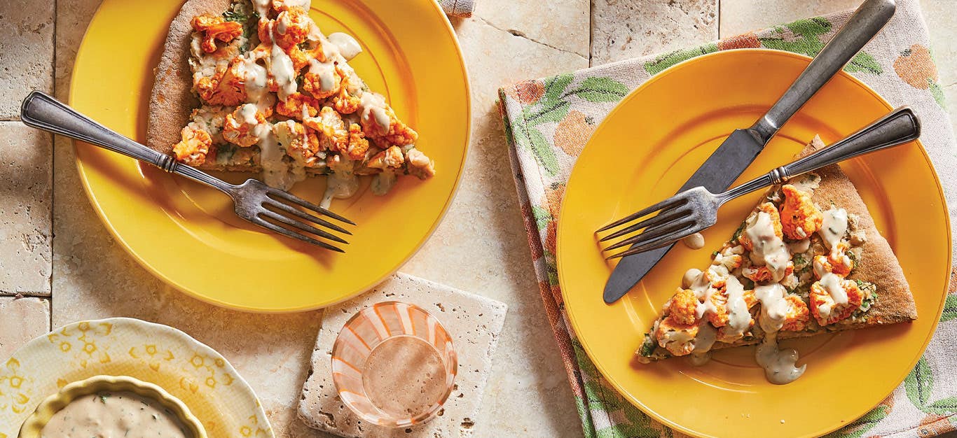 Buffalo Cauliflower Pizza on orange plates with metal knives and forks