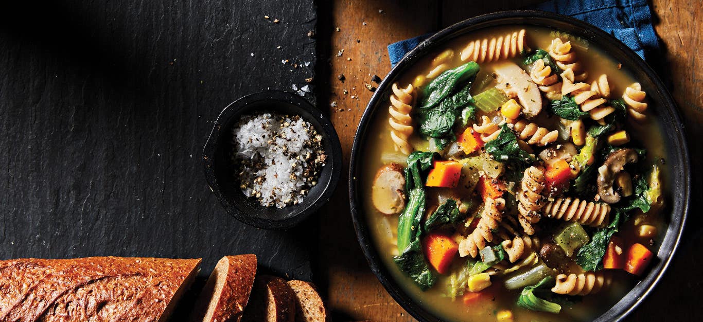 Creamy Vegetable Soup with Escarole in a black bowl next to a loaf of bread and a small bowl of salt