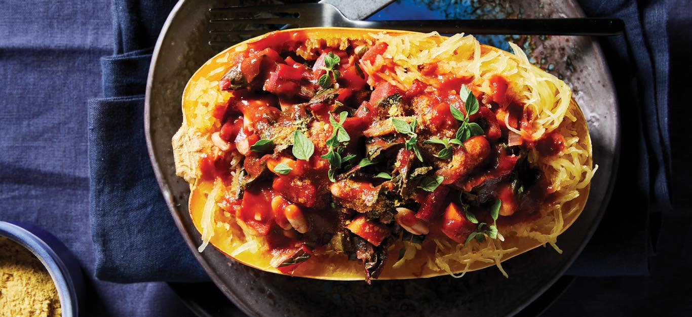 Spaghetti Squash Boats with White Beans and Swiss Chard on a gray ceramic plate against a dark blue tablecloth