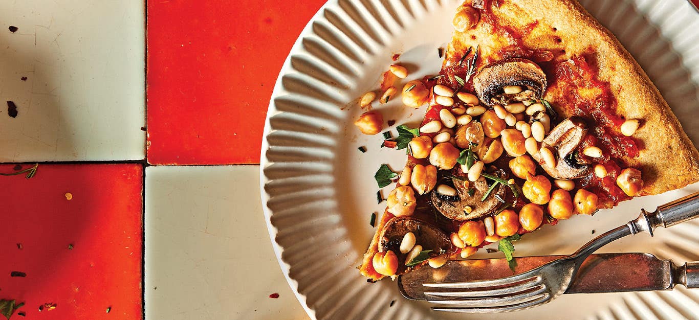 Vegan Mushroom and Chickpea Pizza with Rosemary on a white plate against a red and white checkerboard tile background