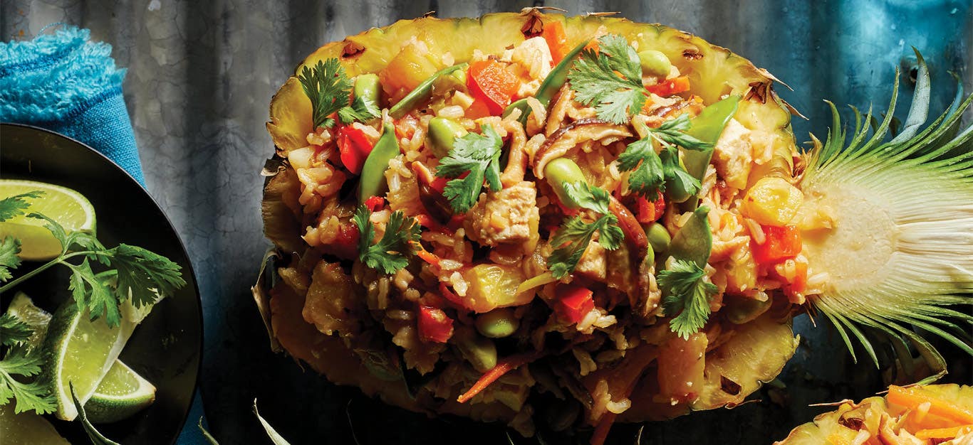 Thai Pineapple Fried Rice served in a hollowed out pineapple half against a dark gray background