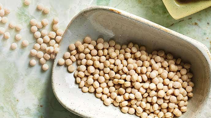 A cream ceramic bowl of Whole wheat couscous, with some couscous spilled onto the counter