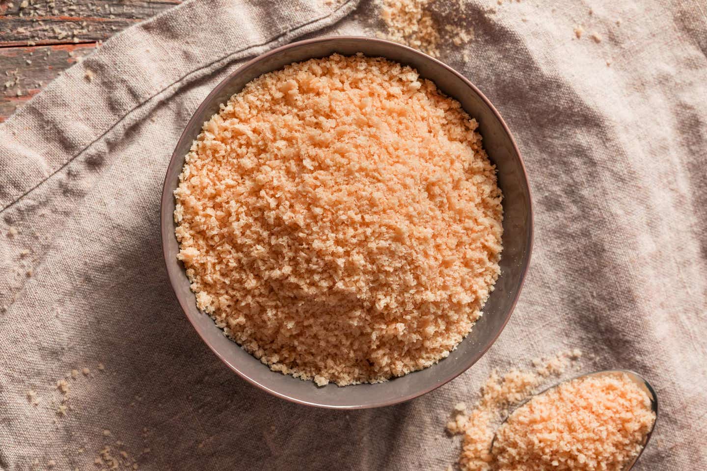 A bowl of whole wheat panko sitting atop a kitchen towel, shown from above