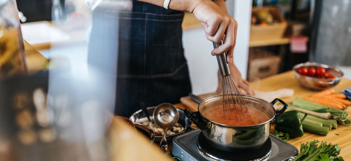 A person stands over a stove thickening a soup