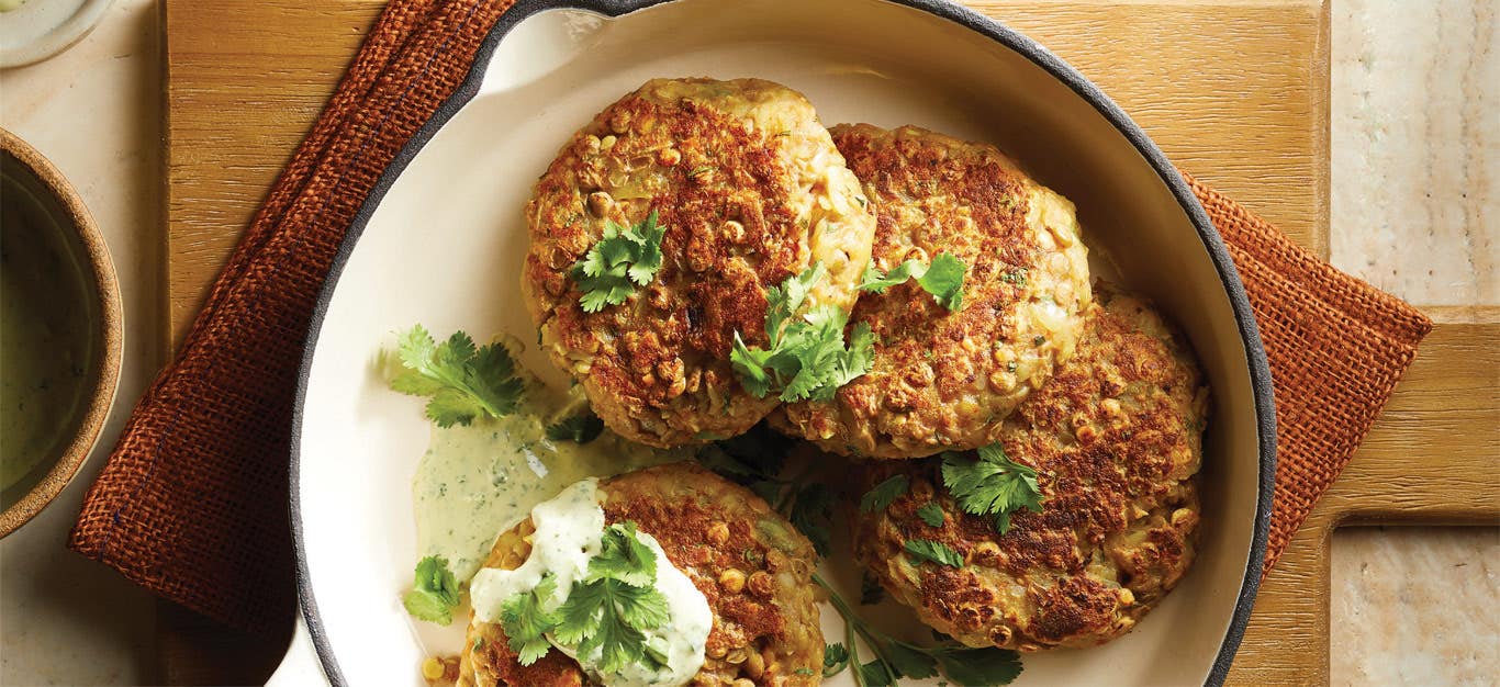 Hash Brown Patties with Green Tahini Sauce and fresh cialntro leaves in a white ceramic bowl sitting on an orange cloth napkin