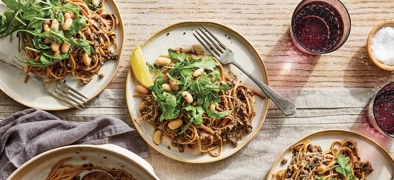 Linguine with Mushroom Pesto topped with arugula on white ceramic plates against a wood tabletop