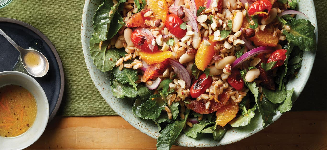 Orange Farro Salad with Pan-Roasted Tomatoes on a light gray plate with a small bowl of mustard dressing to the left side