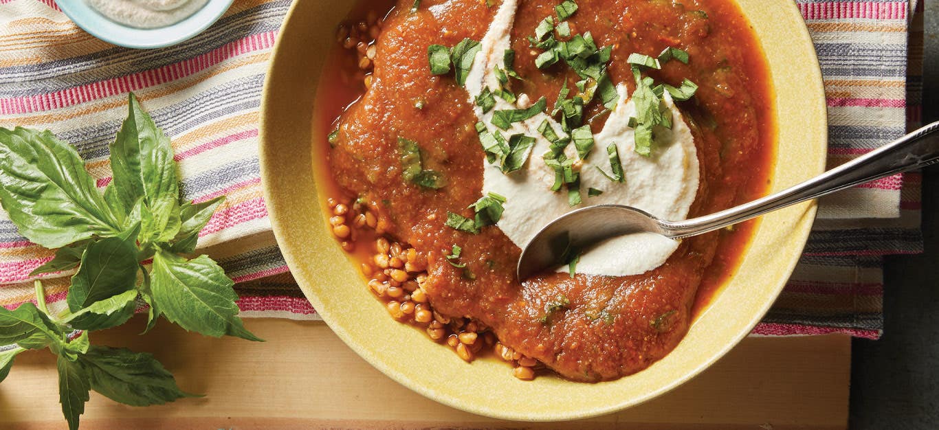 Roasted Tomato and Eggplant Soup in a yellow ceramic bowl with a metal spoon dipped into the soup