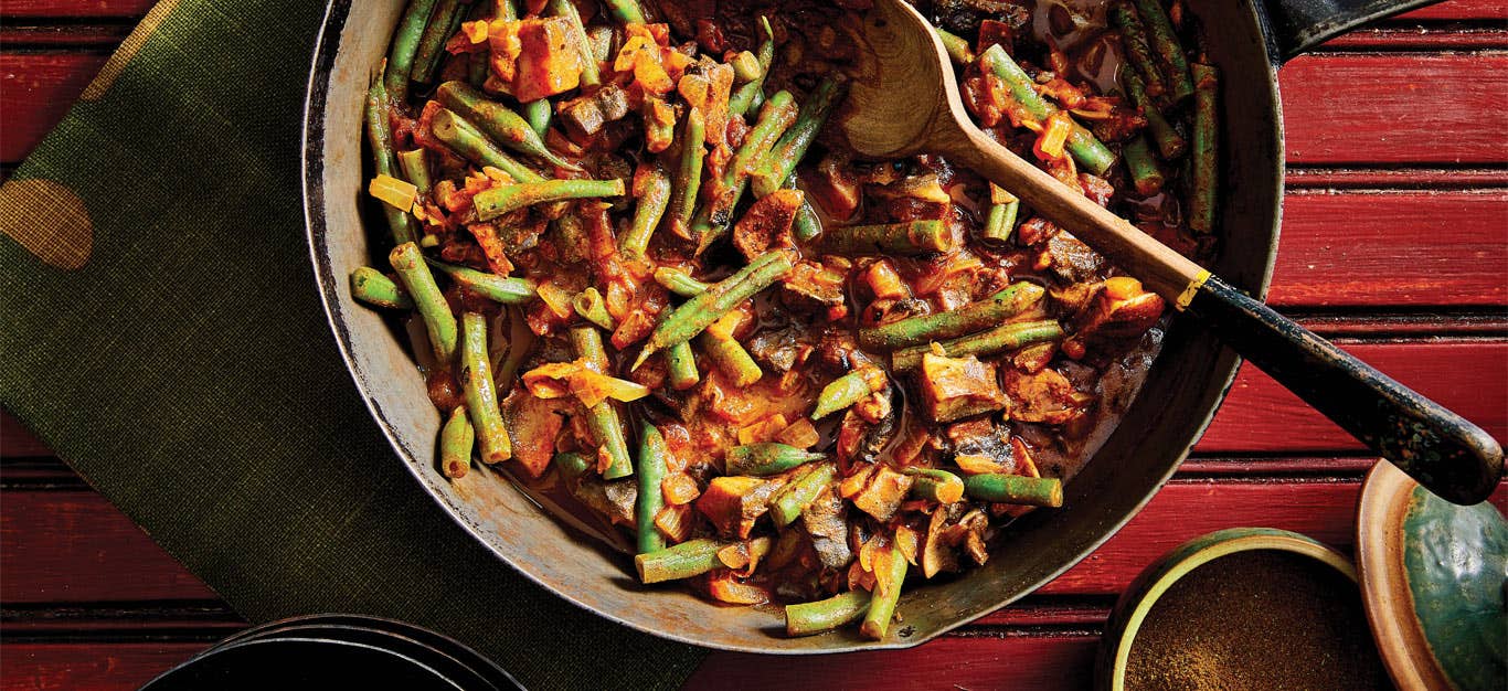 Inguday Tibs (Spicy Ethiopian Mushrooms) in a large metla pot with a wooden spoon against a red wooden background