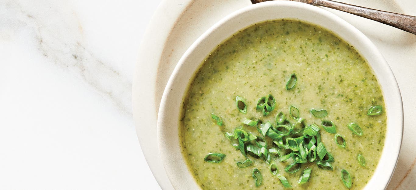 Green Velvet Soup topped with scallions in a white ceramic bowl