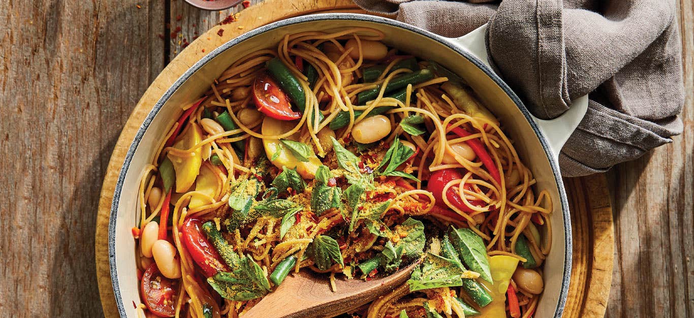 One-Pot Pasta with Spring Veggies in a white Dutch oven sitting on a wooden cutting board