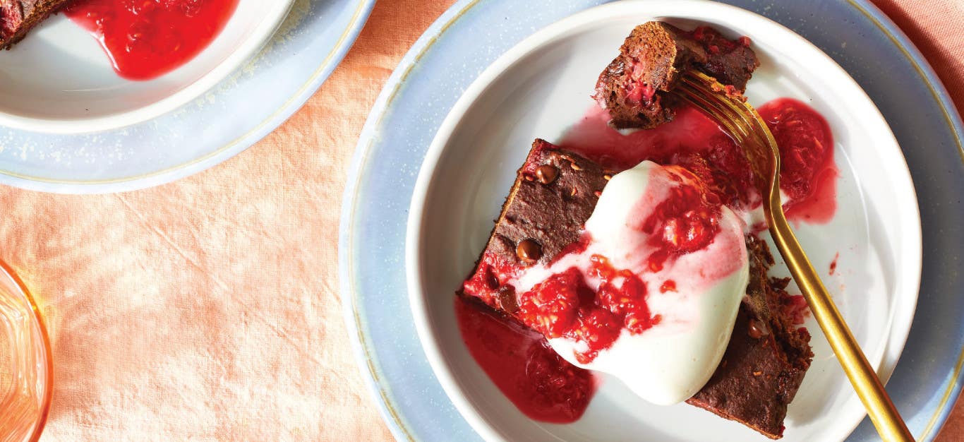 Raspberry Chocolate Cake drizzle with Aquafaba Whipped Cream and fresh raspberries on a pale blue plate on an orange table cloth