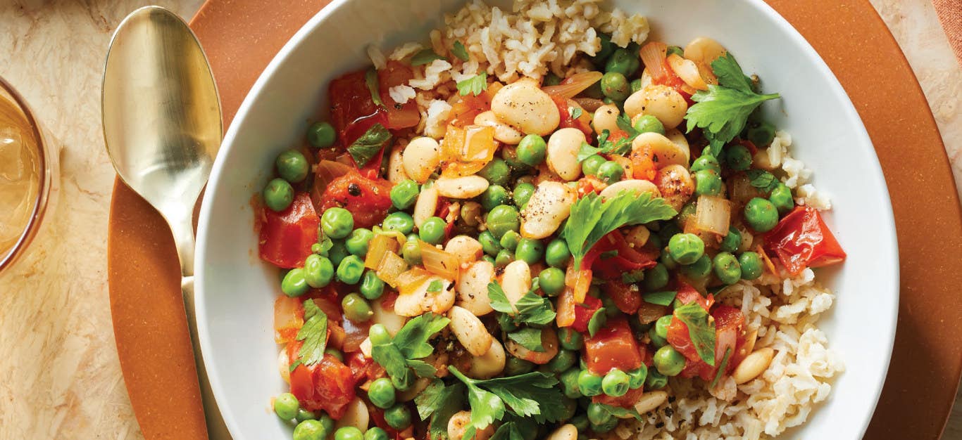 Spanish-Style Fava Beans in a white bowl sitting on a brown plate with a spoon on the side