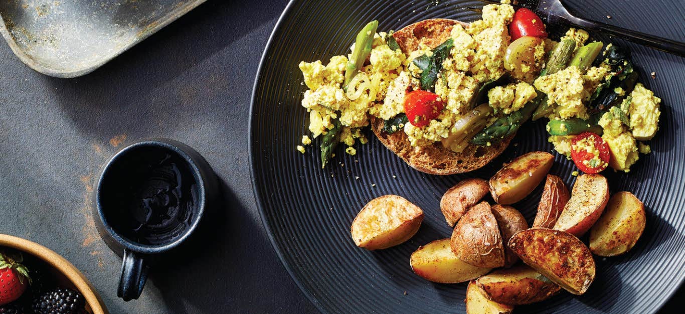 Tofu Veggie Scramble with Roasted Potatoes on a black plate on a dark grey background