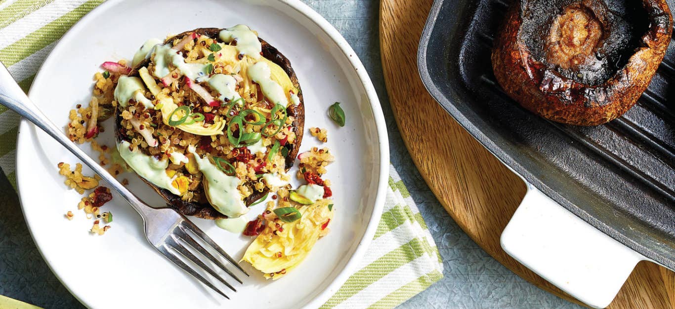 Quinoa- and Artichoke-Stuffed Mushrooms on a white plate sitting on a green and white striped cloth napkin next to a skilleet with one grilled portobello mushroom sitting face up, ready to be stuffed