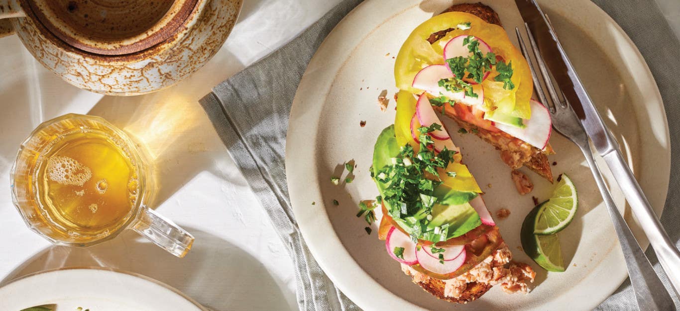 Avocado Toast with Tomato and Spicy Gremolata cut in half on a white plate with a silver knife and fork on the side