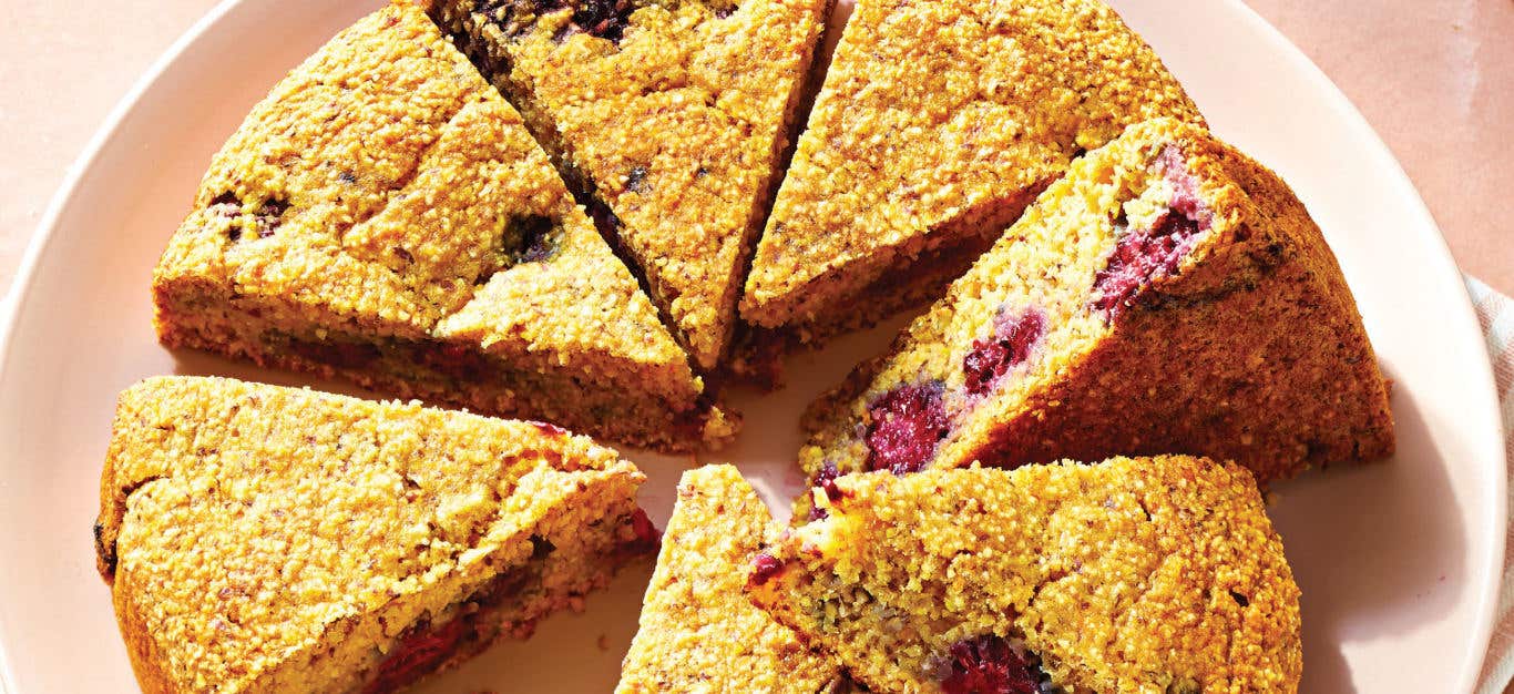 Blackberry Polenta Cake that's been cooked in a circular pan cut into slices, sitting on a pale pink plate