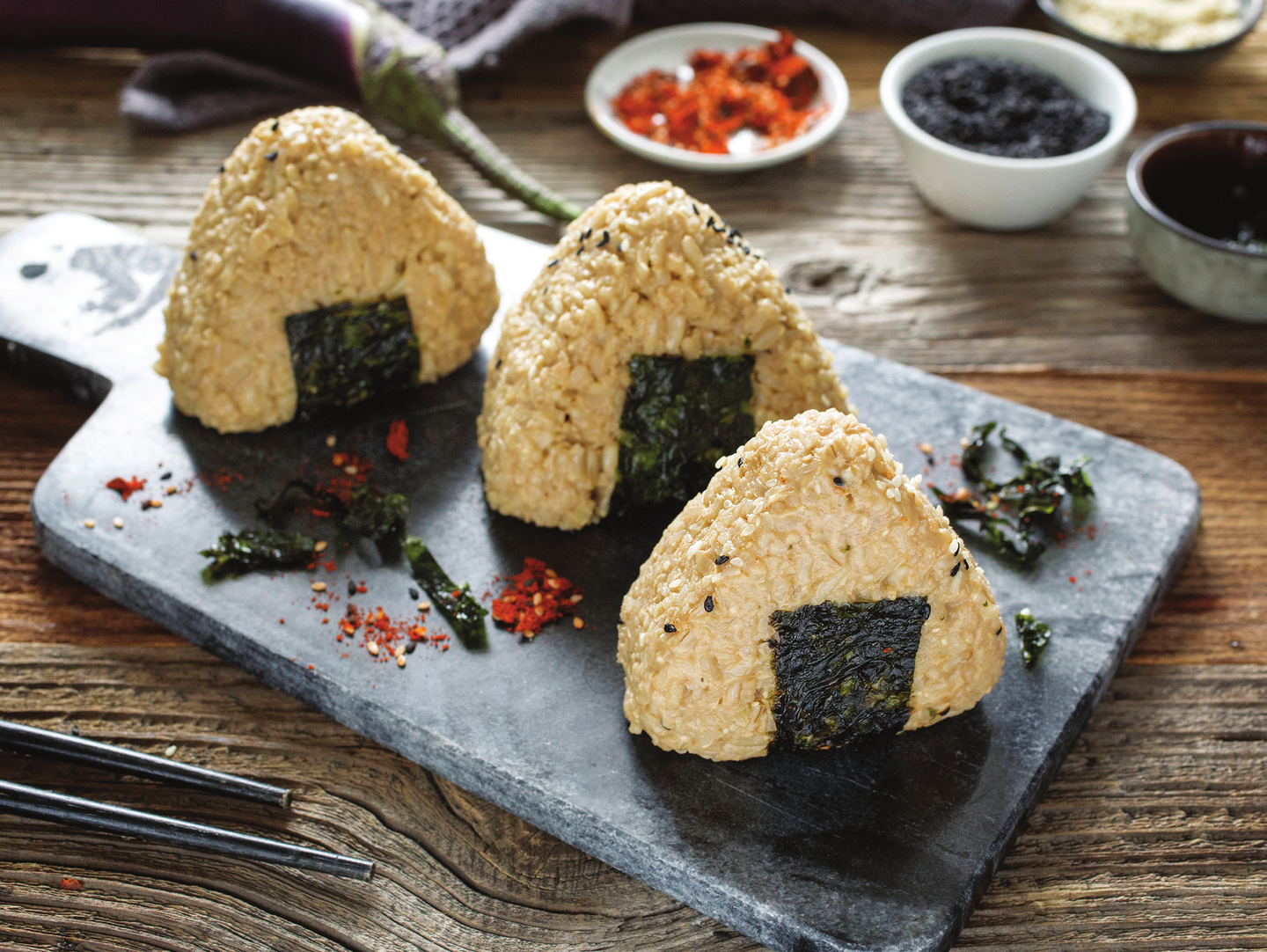 Three triangular brown rice onigiri Japanese rice balls, sprinkled with togarashi and wrapped with nori