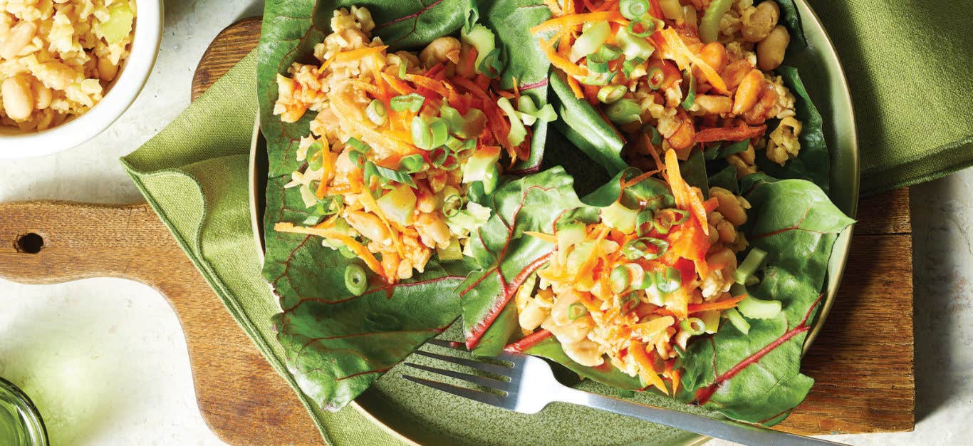 Swiss Chard Wraps with Buffalo Cauliflower Rice on a green plate on a wooden chopping board with a green cloth napkin under the plate