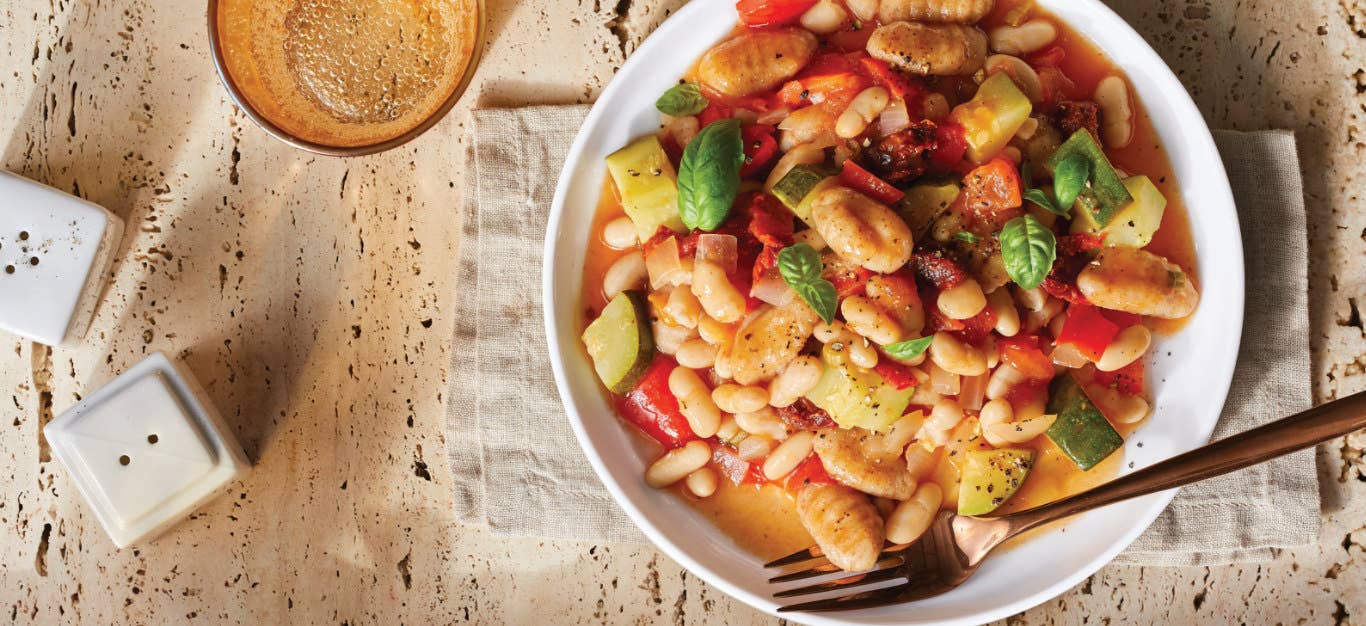 Quick Gnocchi with Zucchini, Tomato, and White Beans in a white pasta bowl on a folded cloth napkin on a light wooden table top