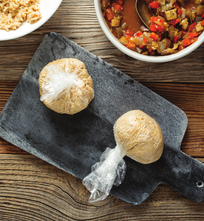 Photo showing the following step for making brown rice onigiri: With the help of the plastic wrap, fold the edges of the rice over the center to cover the filling and form a ball. Twist the plastic to tighten and pack the rice around the filling.