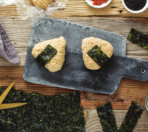 Photo illustrating the following step for brown rice onigiri: To help rice stick together better, let onigiri sit at room temperature for 1 hour. Just before serving, wrap a nori strip around each onigiri. 