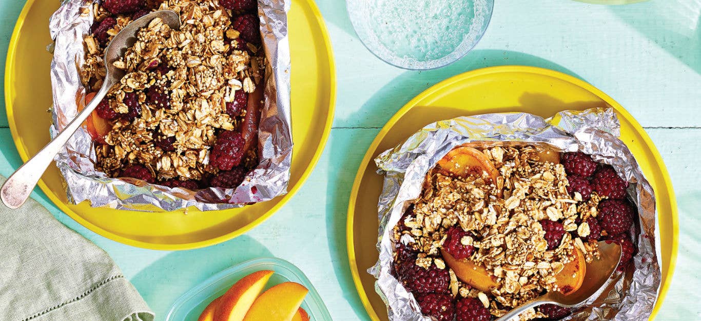 Two Foil-Roasted Blackberry Peach Crisps in tin foil on a yellow plate on a pale blue background