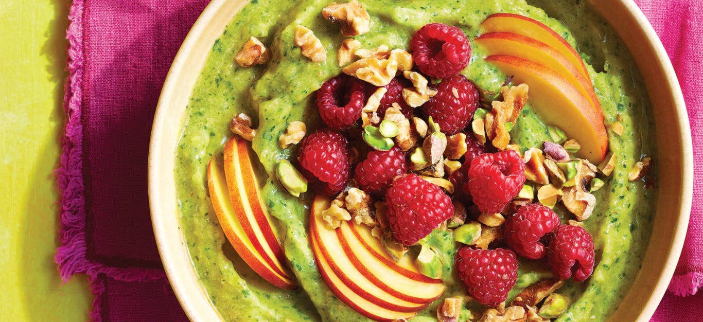 Close-up shot of Arugula and Peach Smoothie Bowl topped with sliced peaches, fresh raspberries and chopped walnuts and pistachios