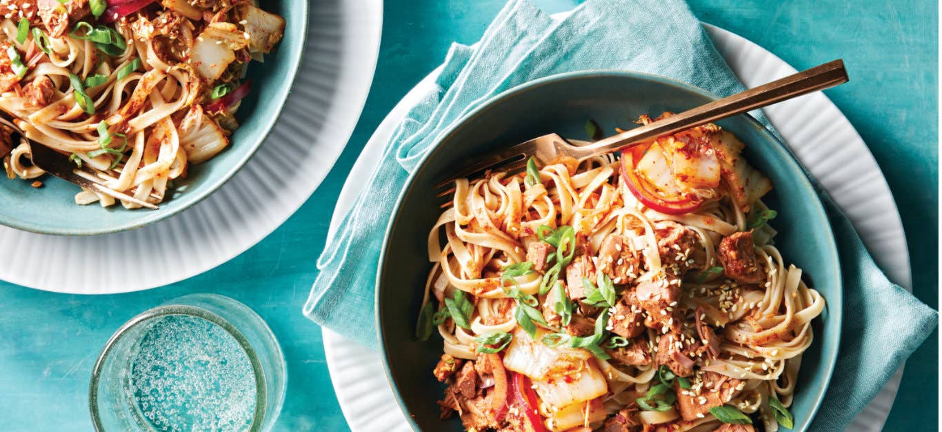 Vegan Bulgogi Noodles with Jackfruit Kimchi in a blue ceramic bowl on a pale blue napkin on a white plate with a fork sitting in the dish