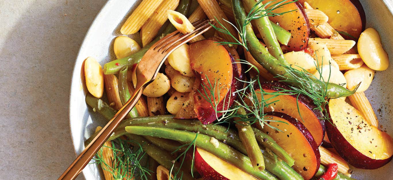 Plum Pasta Salad with Roasted Garlic Vinaigrette in a white bowl with a copper-colored fork