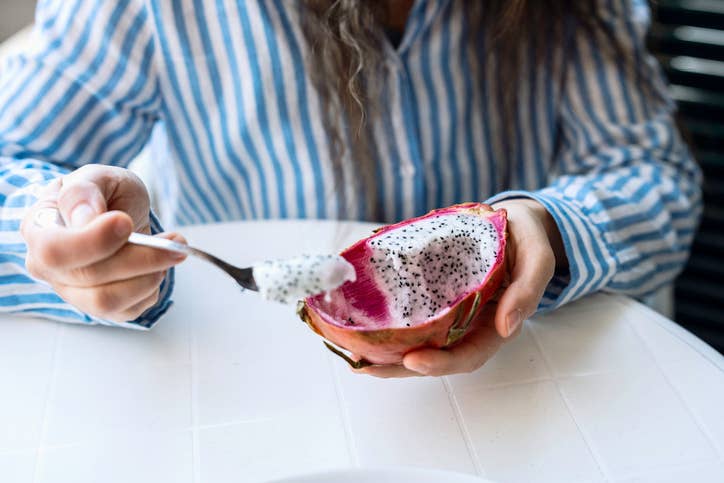 someone scooping out dragon fruit flesh with a spoon