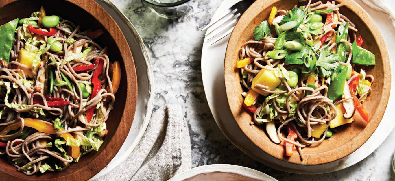 Two bowls of Spicy Cold Noodle Salad with Pineapple, Bell Pepper, and Soy-Lime Dressing in wooden bowls, each sitting on a white dinner late