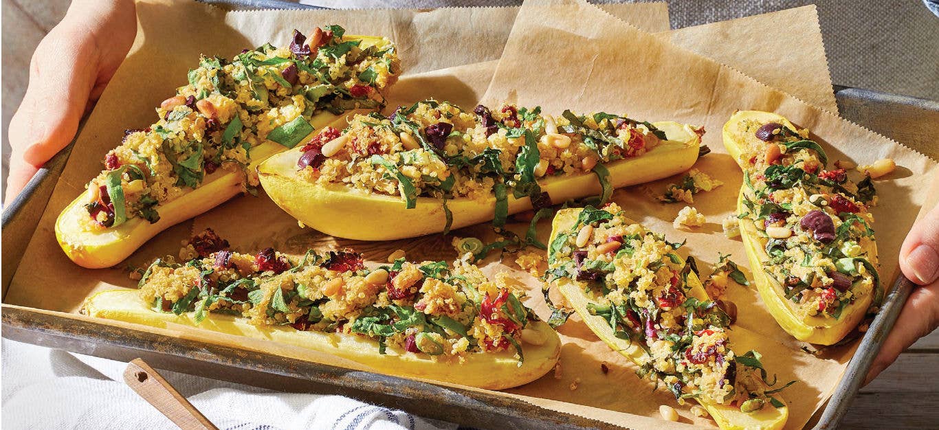 Stuffed Summer Squash with Quinoa, Chard, and Sun-Dried Tomatoes on a baking-paper lined baking tray held by two hands