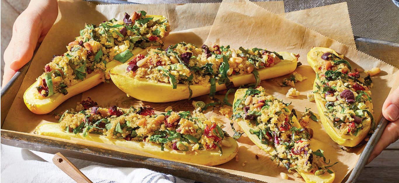 Stuffed Summer Squash with Quinoa, Chard, and Sun-Dried Tomatoes on a baking-paper lined baking tray held by two hands