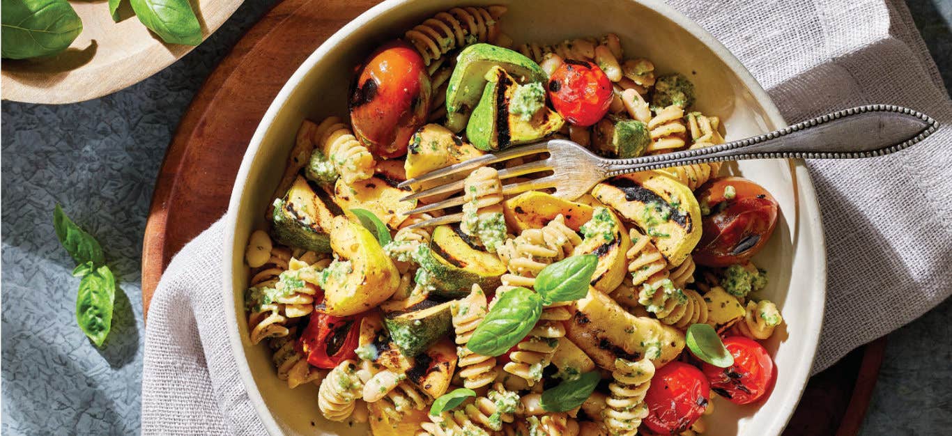 Basil-Leek Pesto Pasta with Cherry Tomatoes and Summer Squash in a white bowl on a cloth napkin in a wooden plate