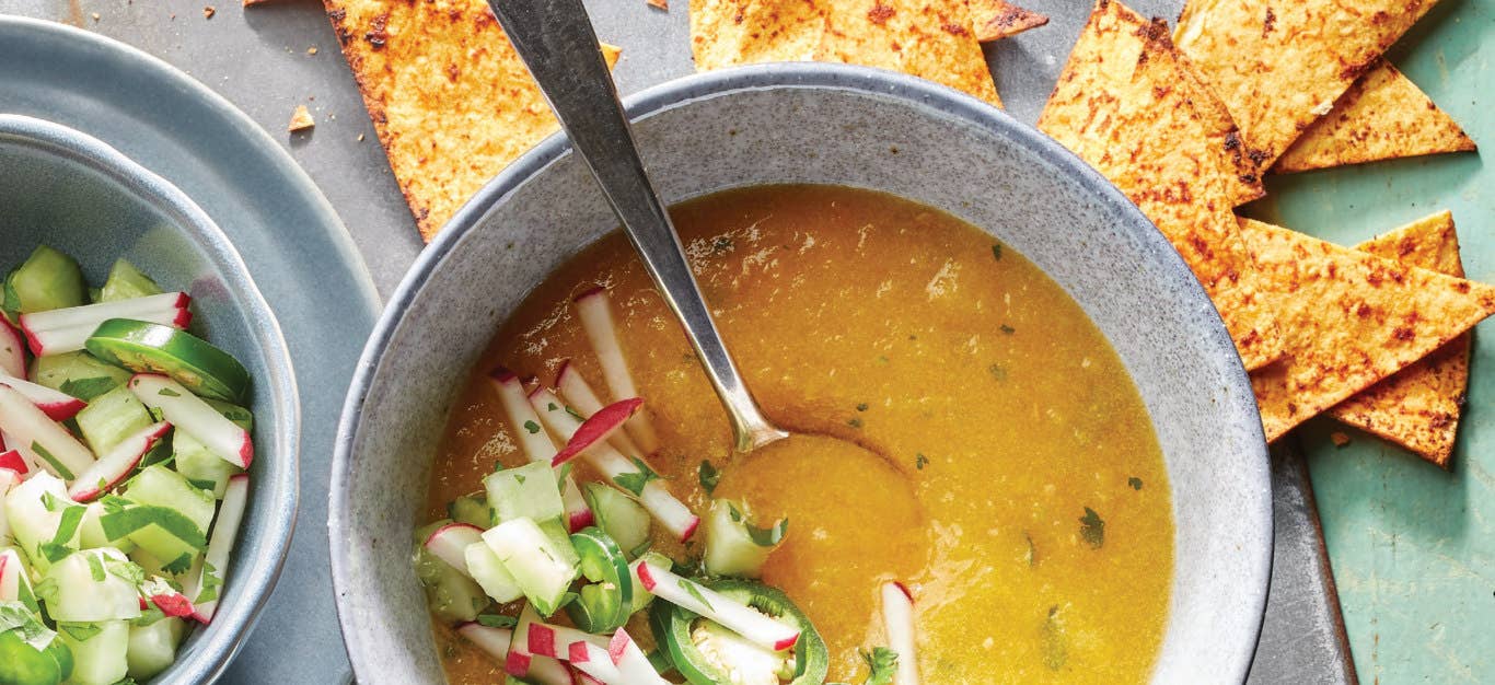 Yellow Tomato and Cucumber Gazpacho in a pale blue ceramic bowl with a handful of Chili-Lime Chips scattered around it