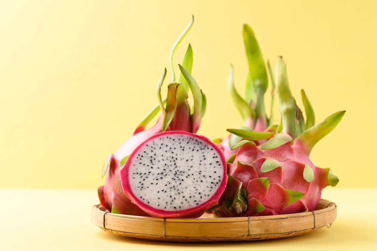Halved fresh dragon fruit in a bamboo basket on yellow background