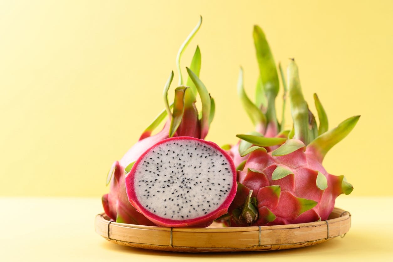 Halved fresh dragon fruit in a bamboo basket on yellow background