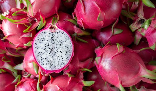 a pile of white dragon fruit with magenta exteriors, with one fruit cut in half to reveal inner white flesh
