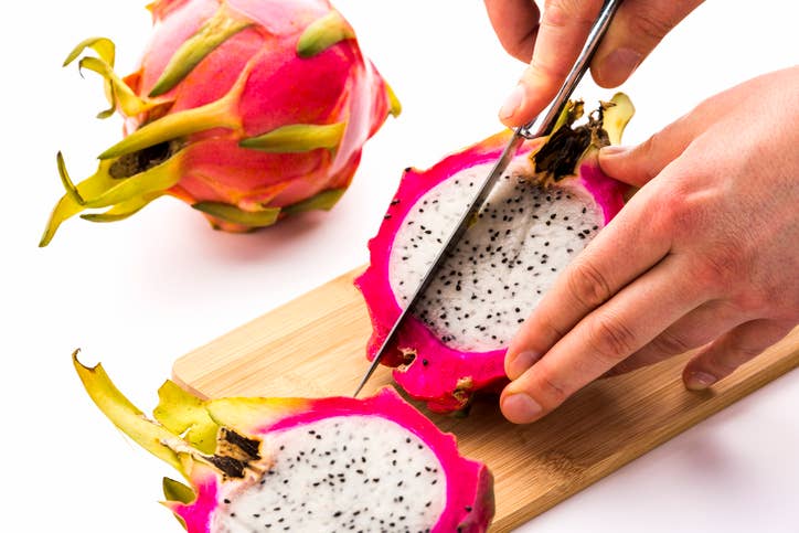 Hands slicing half a dragon fruit into wedges on a cutting board